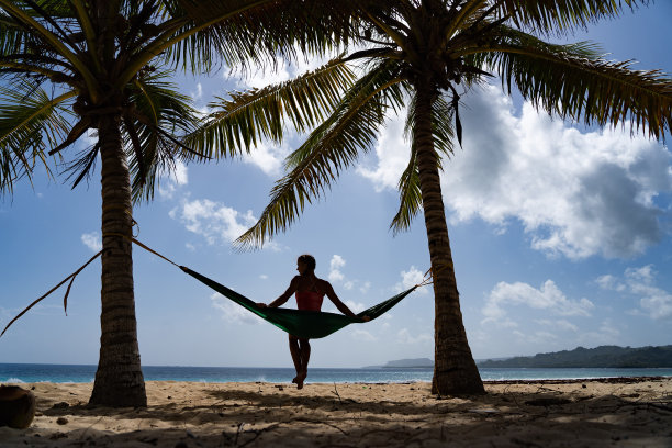 女子在吊床上眺望热带海滩的剪影，度假和旅行概念图片下载