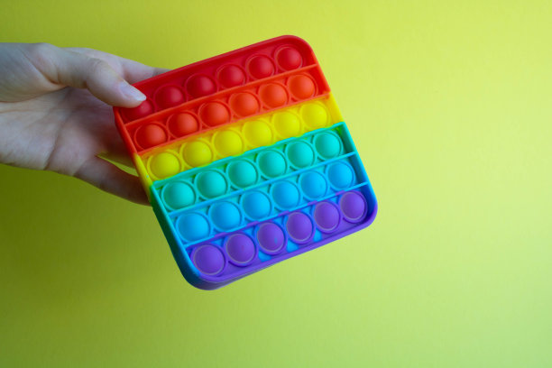 他手里拿着一个感官玩具——一个在黄色背景上坐立不安的玩具。蓝色和橙色有趣的互动抗压力硅胶玩具。文本空间图片下载