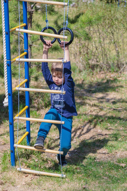 一个金发小孩在操场上玩，挂在吊环上图片下载