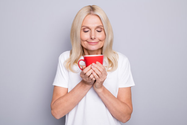 照片肖像的老女人吸入美好的早晨的咖啡捧红的杯子在两只手孤立在灰色的背景图片下载