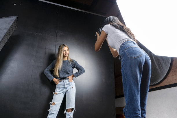 在摄影工作室里，一名模特和一名女摄影师的横向肖像照片，黑色背景。时尚的概念。图片下载