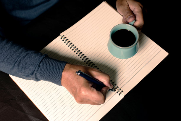 那个男人用钢笔在笔记本上写字，喝着黑咖啡。图片下载