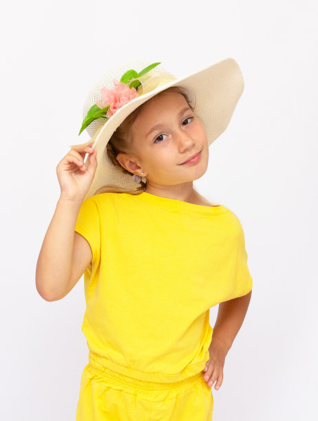 平静的小女孩站在黄色t恤和巴拿马草帽，孤立在白色的背景图片下载
