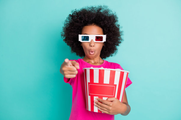 照片肖像惊讶的黑皮肤女孩指着手指电影屏幕上的爆米花孤立在生动的青色背景图片下载