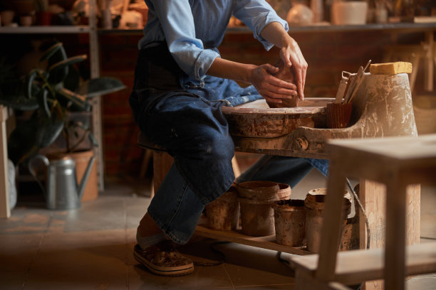 美丽的不知名的手工艺品女人穿着围裙坐在艺术工作室里用一团粘土做东西图片下载