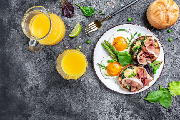 早餐桌上有烤小圆面包、菠菜、芝士、芦笋、火腿、熏火腿和煎蛋。新鲜果汁。俯视图图片下载