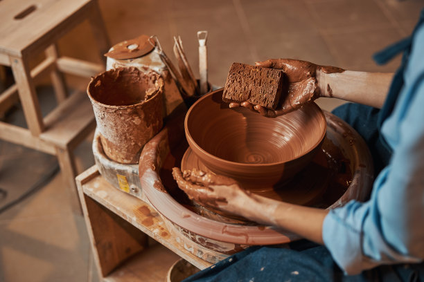不知名的女工匠在艺术工作室的陶轮上挤压新鲜的湿粘土图片下载