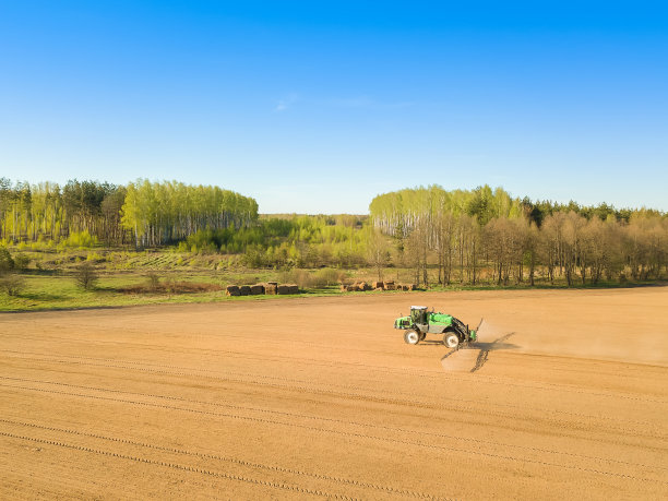 这是一辆拖拉机在春天向森林附近的大片田野里的土壤喷洒化肥和化学物质的无人机图像图片下载