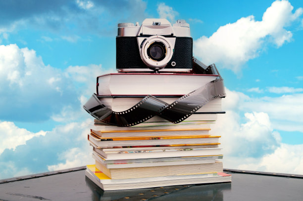 模拟相机，在蓝天的映衬下，一卷胶卷叠在一堆书上。旧相机堆在书上。模拟电影带。图片下载