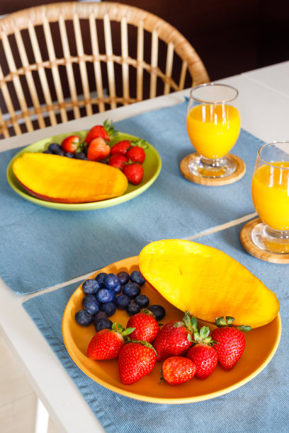 一顿健康的饭菜，两盘新鲜的草莓、芒果和蓝莓，还有厨房桌上的橙汁。良好的热量，适当的营养，吃水果，垂直照片图片下载