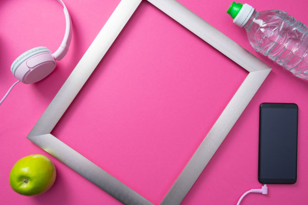 金属框架，带耳机的手机，一瓶水和绿苹果在普通的粉红色背景图片下载