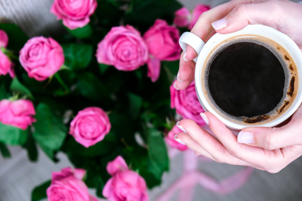 一杯咖啡和粉红玫瑰。节日概念，生日时送一束玫瑰，早餐时送一束鲜花。女性手握卡布奇诺图片下载