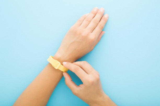 黄色防蚊带戴在年轻的成年妇女手腕上，浅蓝色的桌子背景。柔和的颜色。特写镜头。视角拍摄。防止昆虫。自顶向下的观点。图片下载
