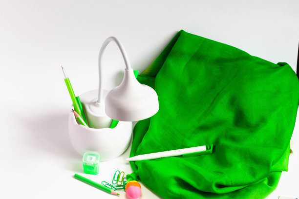 漂亮的灯与一个隔间储存绿色文具。绿色的钢笔，铅笔，毡尖笔，回形针，卷笔刀都在一张白色的桌子上，绿色的布图片下载