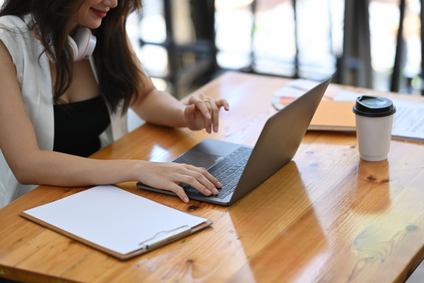 剪短的照片，年轻的女性自由职业者戴着耳机和工作与笔记本电脑在木桌子上。图片下载