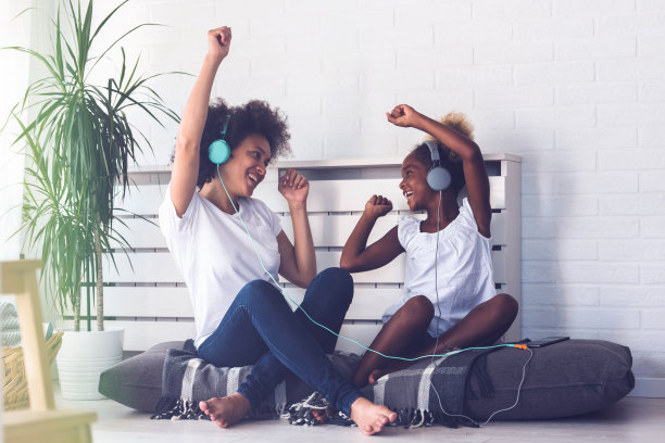 美丽微笑的非洲裔美国母亲和女儿有乐趣在家里听音乐耳机图片下载