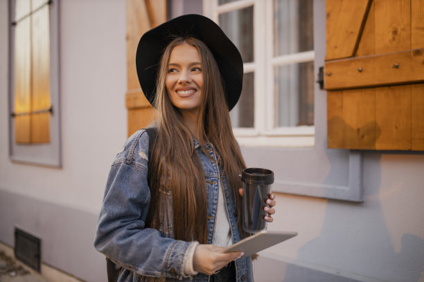 年轻女子喝着咖啡，在街上用着平板电脑图片下载