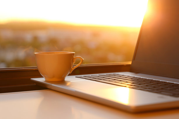 舒适的工作场所在家庭办公室，热咖啡杯和笔记本电脑在桌子上对着窗户在日出图片下载