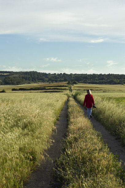 一名妇女穿着一件难以辨认的红色夹克，走在谷地的路上图片下载