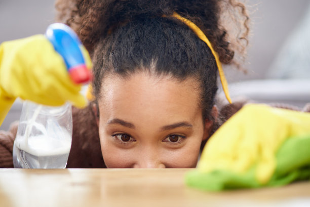 照片中，一名妇女戴着手套，拿着喷雾器，在家里清洁木质表面图片下载