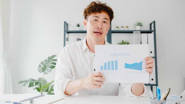 亚洲商人在新常态下保持社交距离以预防病毒，在办公室工作时看着摄像机向同事介绍计划。图片下载