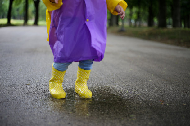 闭上孩子的腿，穿着黄色的胶靴，在水坑里跳在秋天的散步库存照片图片下载