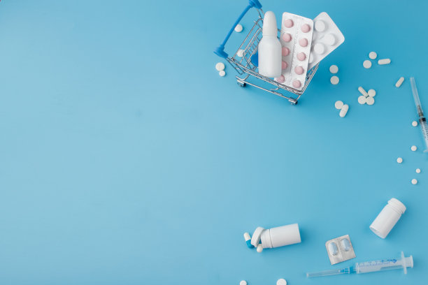 蓝色背景上散落着各种药片、药品、喷雾、瓶子、温度计、注射器和空的购物车。药房购物的概念图片下载