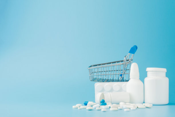 蓝色背景上散落着各种药片、药品、喷雾、瓶子、温度计、注射器和空的购物车。药房购物的概念图片下载