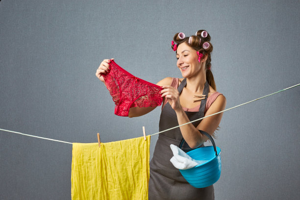 一个漂亮的复古女人的肖像挂在灰色背景上的一串内裤。家庭主妇范妮戴着卷发器烘干衣服。家庭的概念。图片下载