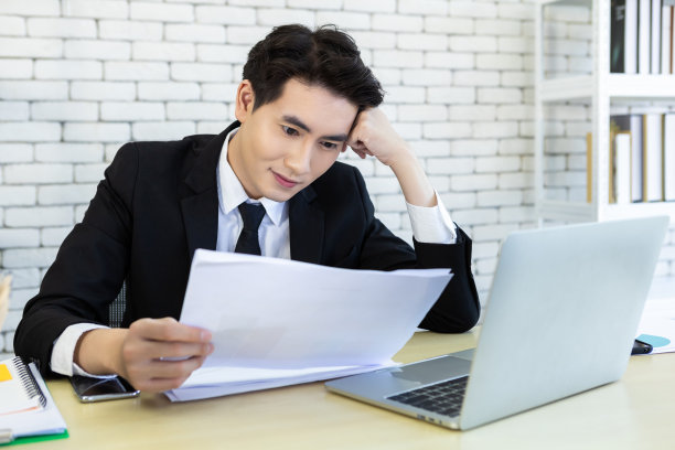 成功的亚洲青年商人乐强调了在办公室背景的木桌上看到了一份商业计划书和笔记本电脑的文件。图片下载