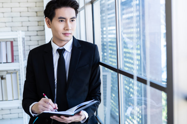 快乐成功的亚洲年轻商人与阅读记录在商业计划笔记本看着窗户在办公室的背景图片下载
