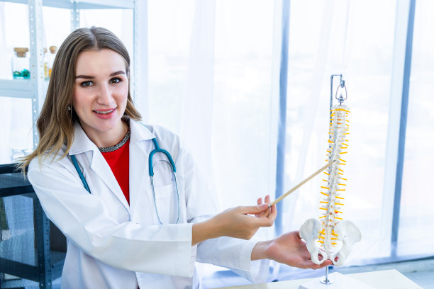 特写的女性医生治疗与听诊器指向脊柱模型与积极的情绪在医院背景。图片下载