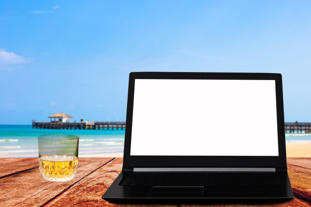 旧木桌上放着笔记本电脑，白色的屏幕和一个威士忌酒杯图片下载