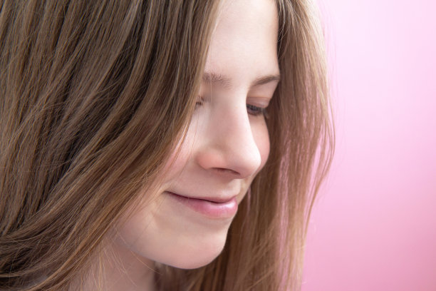 一个美丽的微笑少女的脸与长头发在粉红色的背景图片下载