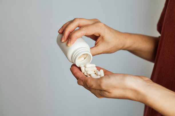 妇女将药丸或维生素从罐子里倒在手上。服用维生素或药物。保健、医药、药房、预防疾病的概念。手里拿着药丸或维生素的罐子图片下载