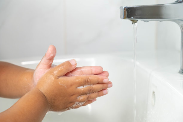 这是一张女孩的手的照片。在浴室的白色水槽上用白色泡沫肥皂洗手。图片下载