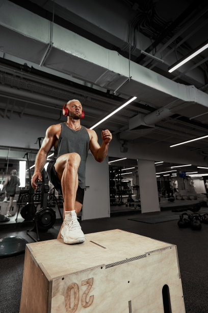 性感的肌肉男使用平台为他的腿在一个黑暗的彩色背景的健身房图片下载