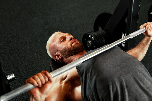 一个肌肉发达的男人在健身房练杠铃的特写。残忍的健美运动员运动员有六块腹肌，完美的腹肌，肩膀，二头肌，三头肌和胸部图片下载
