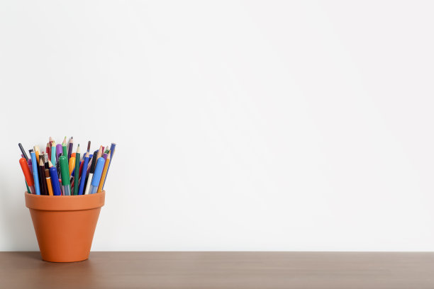 白色的墙壁，木制的桌子上放着铅笔和文具。工作、学习、学校背景理念。图片下载