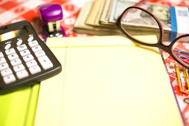 厨房桌子上有记事本，计算器，现金，眼镜，回形针和订书机。计算再融资决策。图片下载