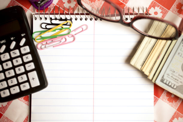 厨房桌子上有记事本，计算器，现金，眼镜，回形针和订书机。计算再融资决策。图片下载