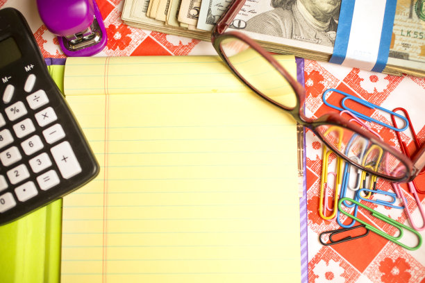 厨房桌子上有记事本，计算器，现金，眼镜，回形针和订书机。计算再融资决策。图片下载