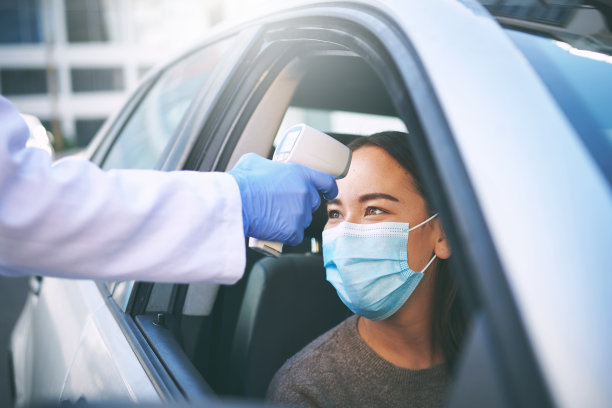 一个戴着面具的年轻女子坐在她的车里让医生检查她的体温图片下载