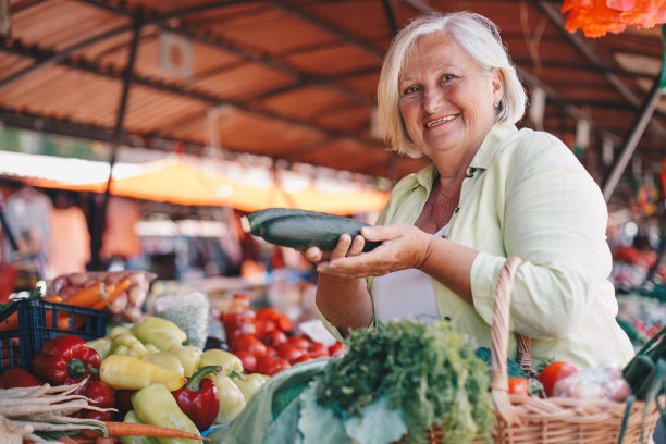 老妇人把黄瓜放进购物篮。图片下载