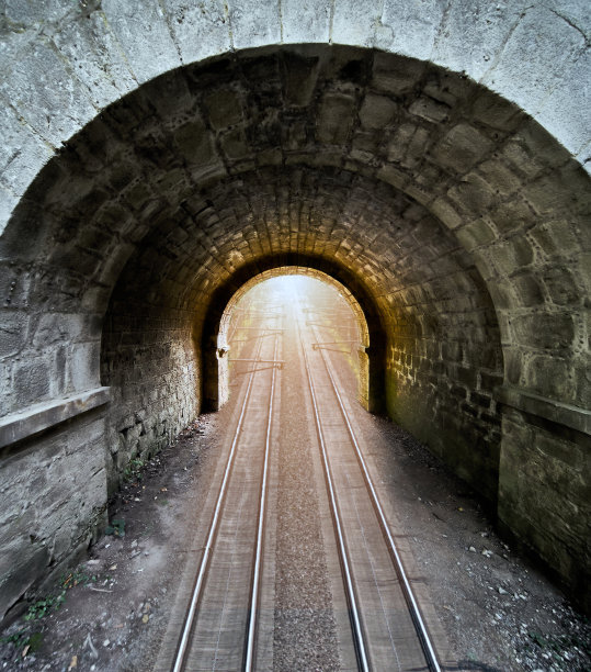 粗糙的石头和一个圆形拱门组成的黑暗通道，其中有两条铁路线，构成了一种超现实的形象图片下载