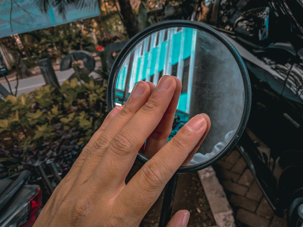 一个穿着白色夹克的男人拿着一个圆形的彩色摩托车后视镜在白天拍摄图片下载