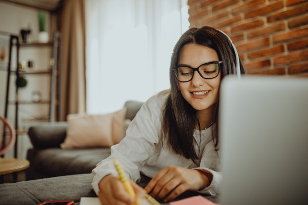 一位年轻的女学生坐在沙发上使用笔记本电脑耳机学习图片下载