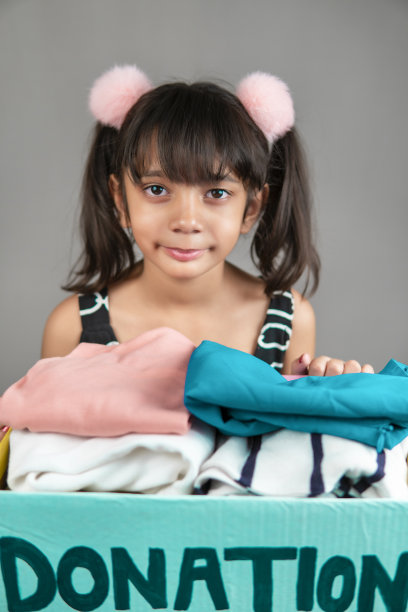 小女孩拿着一个捐赠箱，里面装满了捐赠的旧衣服。图片下载