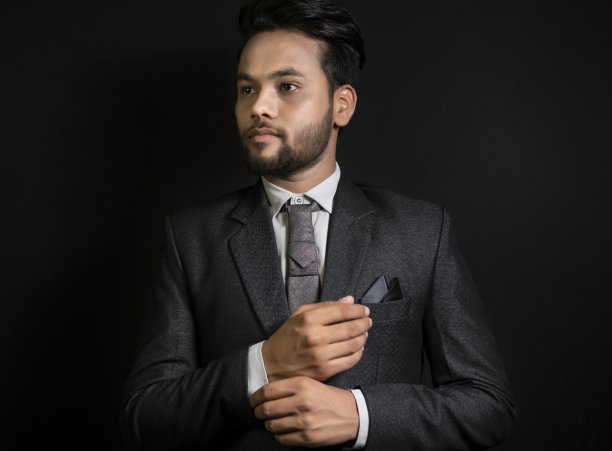 低调肖像英俊的印度年轻商人固定袖扣他的西装。图片下载