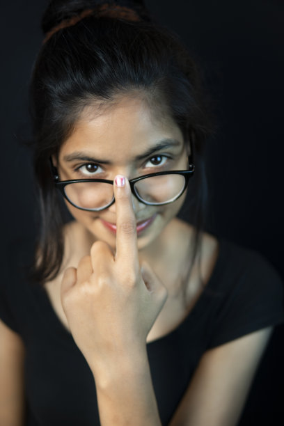 高角度的特写肖像，一个戴眼镜的快乐的年轻女子看着她的眼镜。图片下载